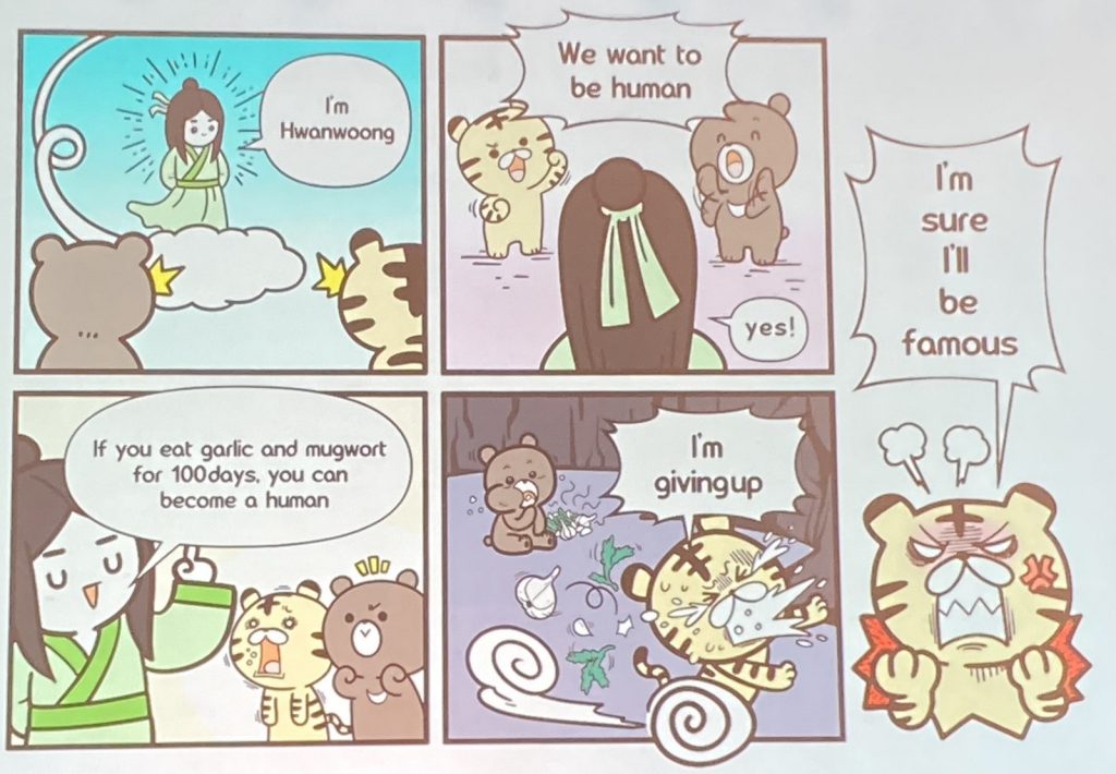 A man descends on the sky to a bear and a tiger. "I'm Hwanwoong" he says. The tiger and bear both say, "We want to be human," to which the man says, "Yes! If you eat garlic and mugwort for 100 days, you can become a human." The tiger runs out of the cave yelling "I'm giving up," leaving a trail of herbs and garlic. On the right side of the image, the angry tiger says, "I'm sure I'll be famous."
