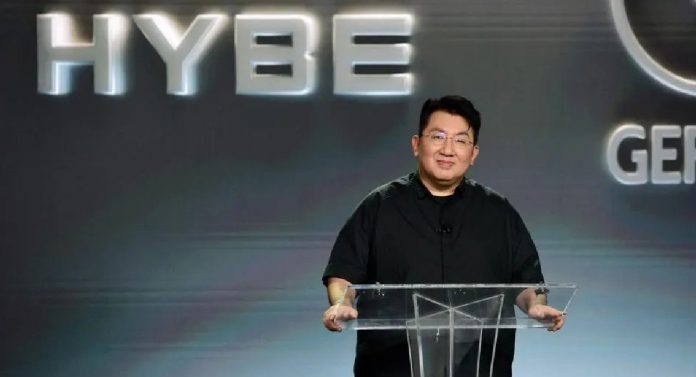 Bang Si-hyuk stands behind a podium in front of the HYBE logo