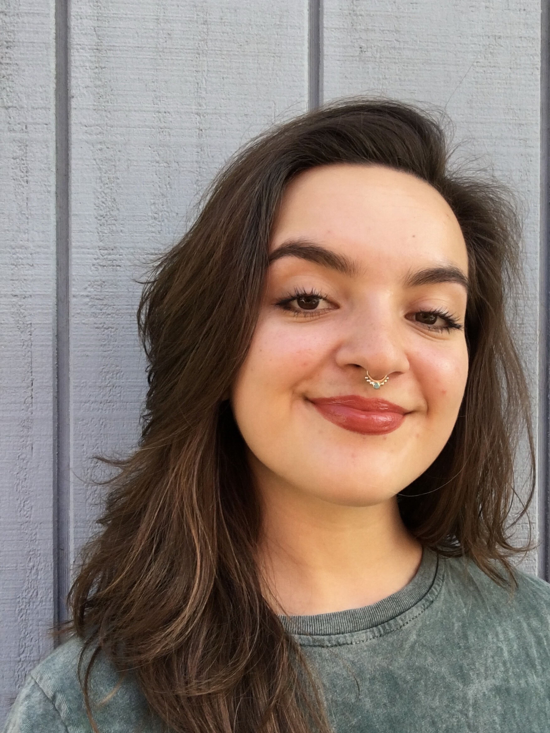 A headshot of WEBTOON Senior Editor, Sonia Tagari. Standing in front of a gray concrete wall with a confident smile. 
