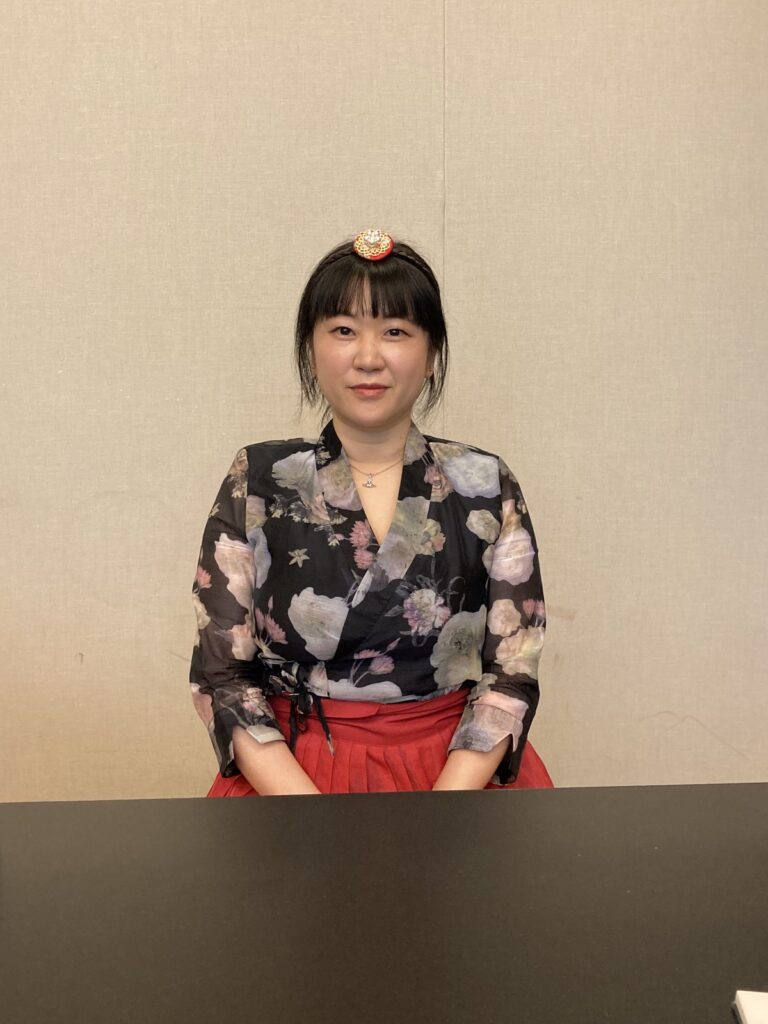 A photograph of Park Seulki Rhea. She is wearing a flower-printed blouse and a red skirt.