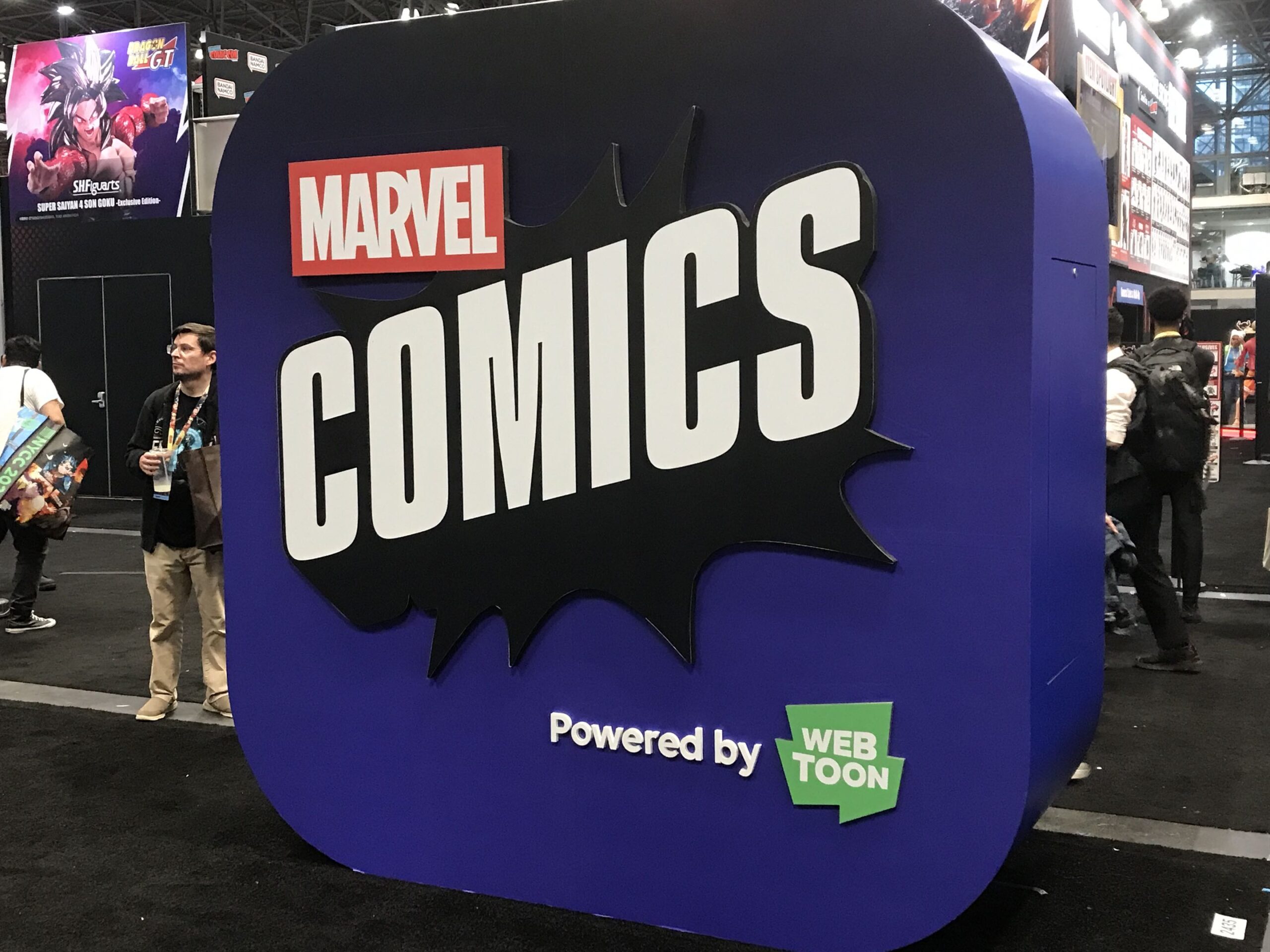 another version of the Marvel Comics app logo on a dark blue stand in New York Comic Con. The powered by Webtoons text on the bottom right of the display.
